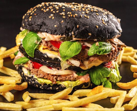 Close-up, black burger with two cutlets, cheese, vegetables and herbs and french fries